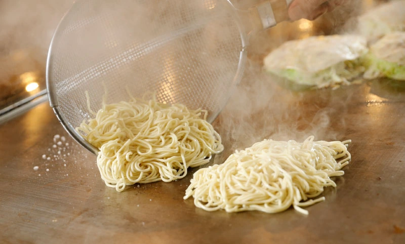 ざるから鉄板へ、みっちゃんの生麺が落ちていく
