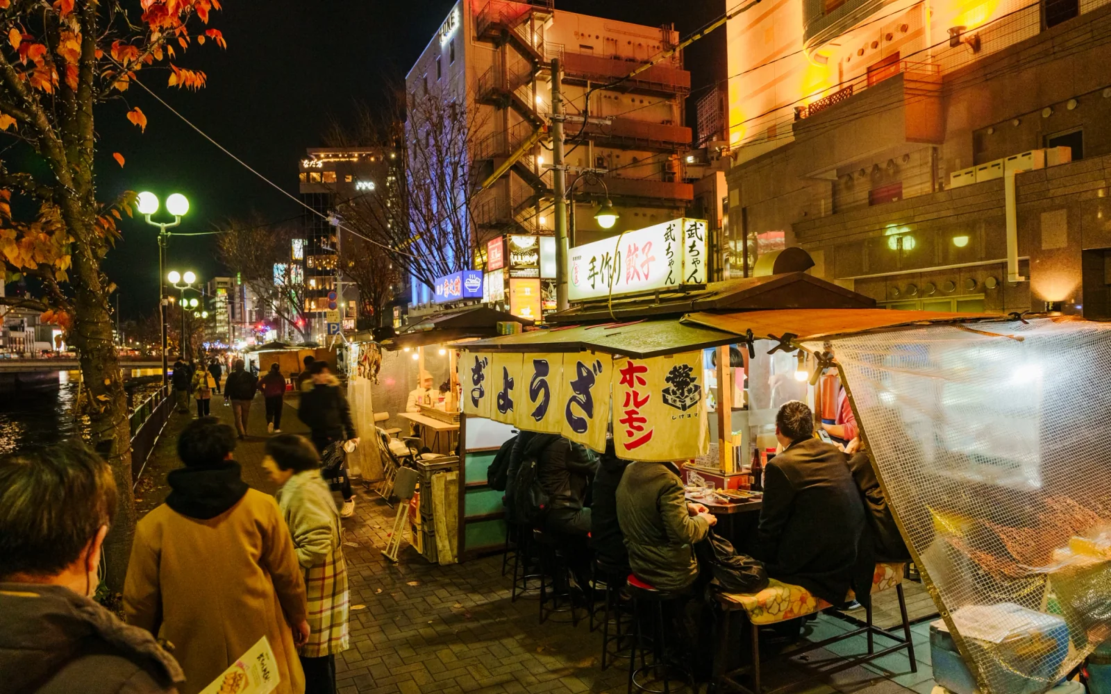 Row of illuminated Hakata Yatai food stalls along the Naka River at twilight in Fukuoka