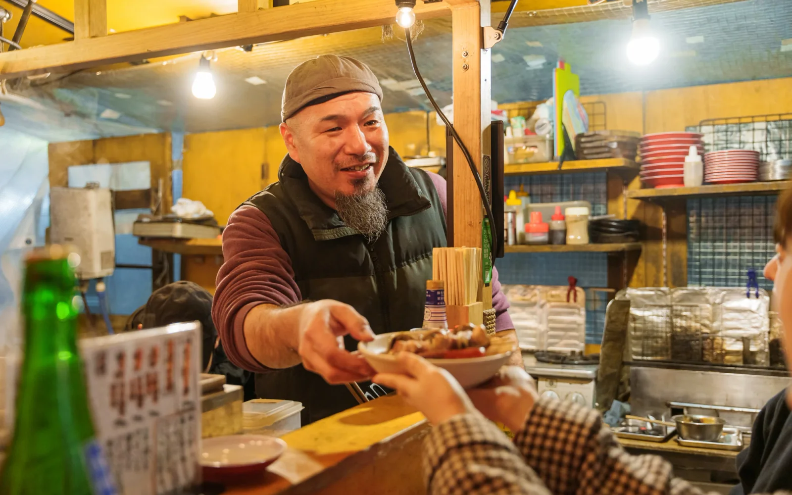 Yatai master preparing noodle baskets behind a steaming wooden counter with seated diners in Fukuoka