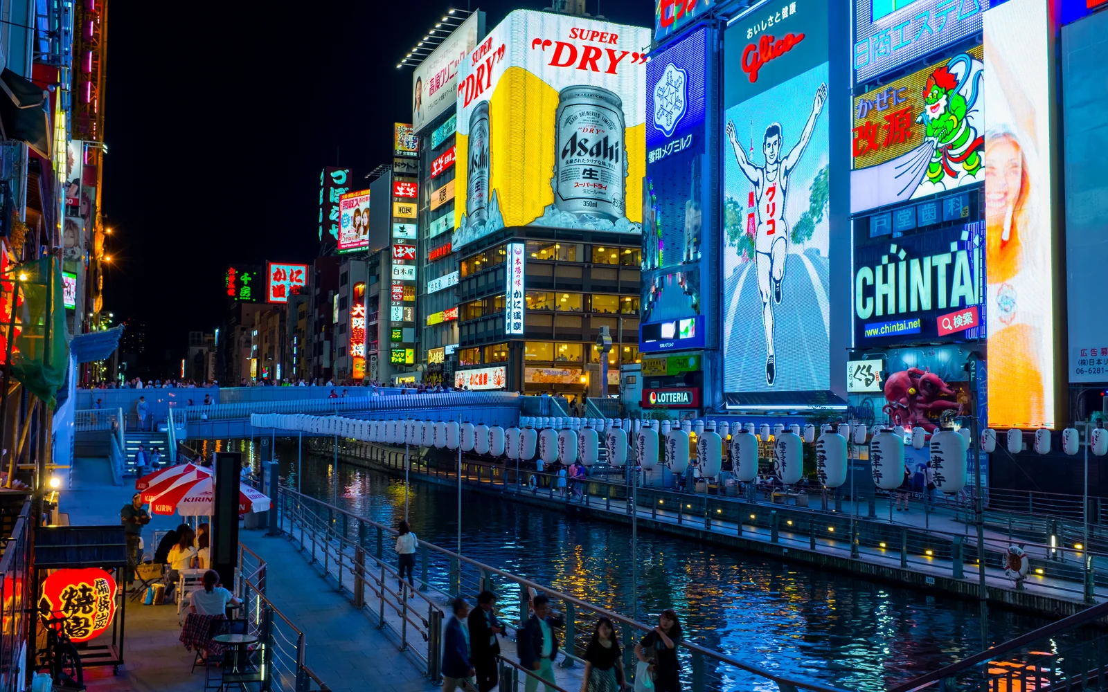 Illuminated Dotonbori canal with giant neon billboards, bustling street crowds, and vibrant bridges in Osaka at dusk