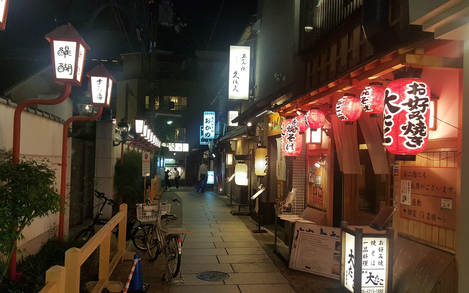 Traditional cobblestone alleyway of Hozenji Yokocho glowing with red paper lanterns and cozy drinking taverns at night