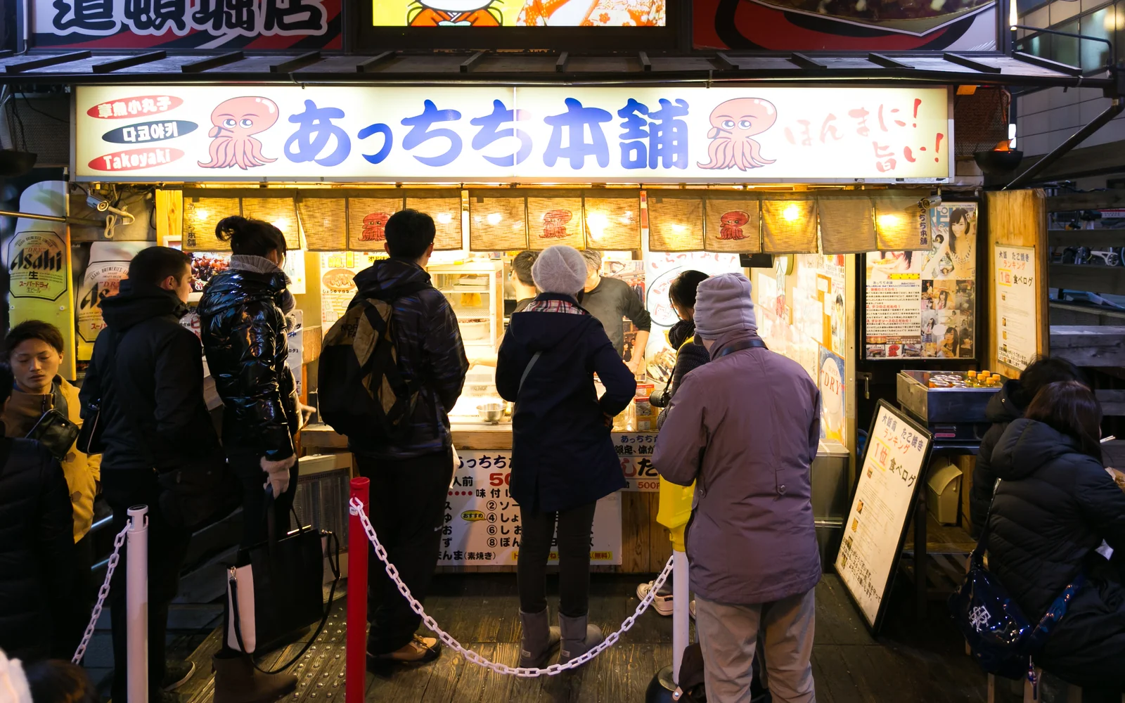 Artisan using twin metal picks to turn piping hot takoyaki spheres on a sizzling cast-iron griddle in Osaka