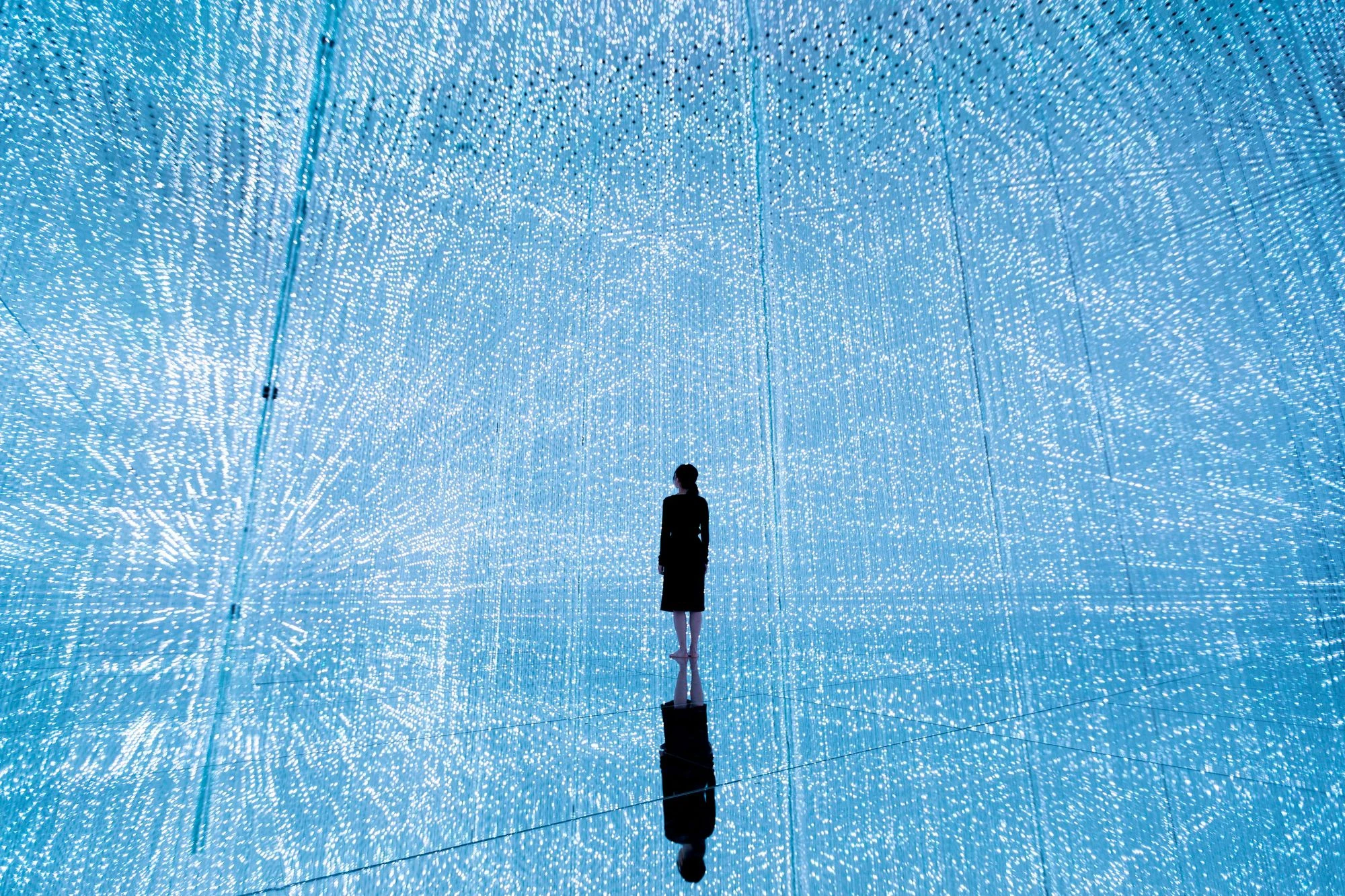 A visitor surrounded by blue points of light in The Infinite Crystal Universe at teamLab Planets.