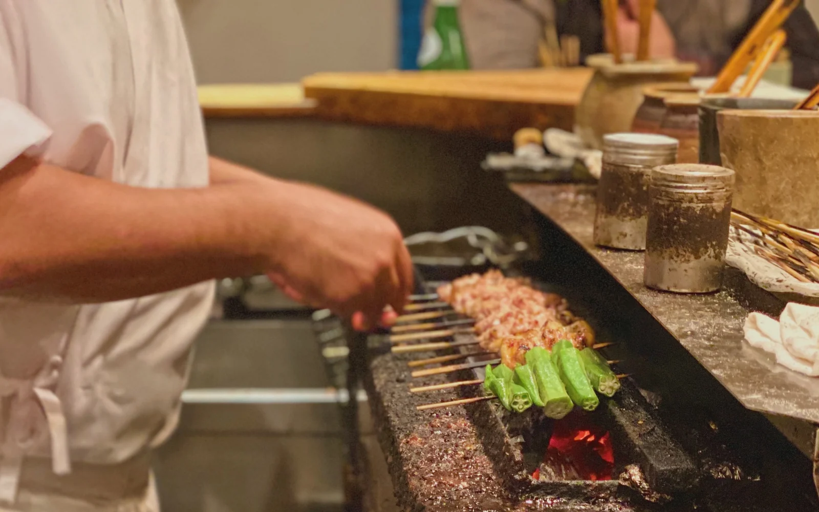 Master yakitori itamae fanning glowing Kishu Binchotan charcoal grill with chicken skewers sizzling